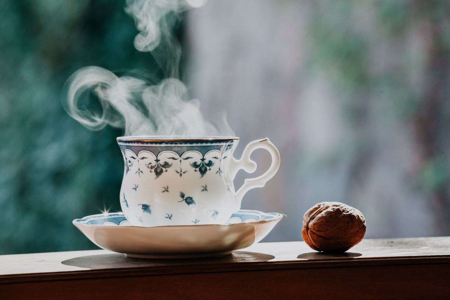 Une tasse de thé fumante posée sur une table en bois sur un balcon ensoleillé avec une vue sur la ville.