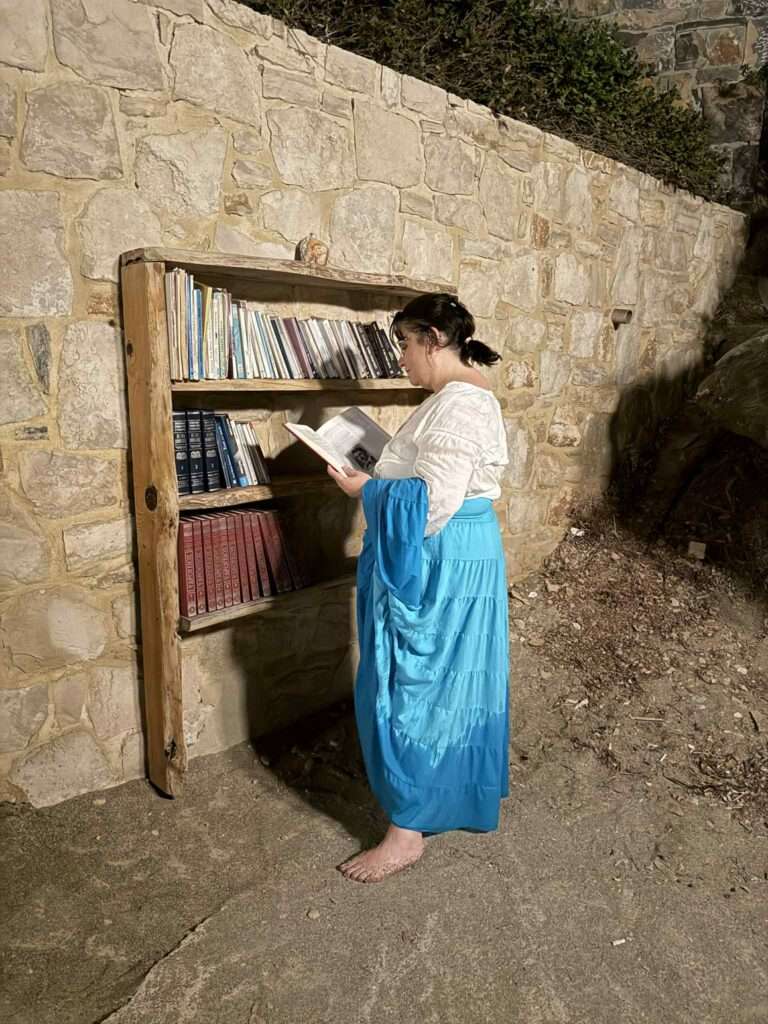 Maria lisant un livre devant une bibliothèque de pierre et de bois, un soir d'été en Crète