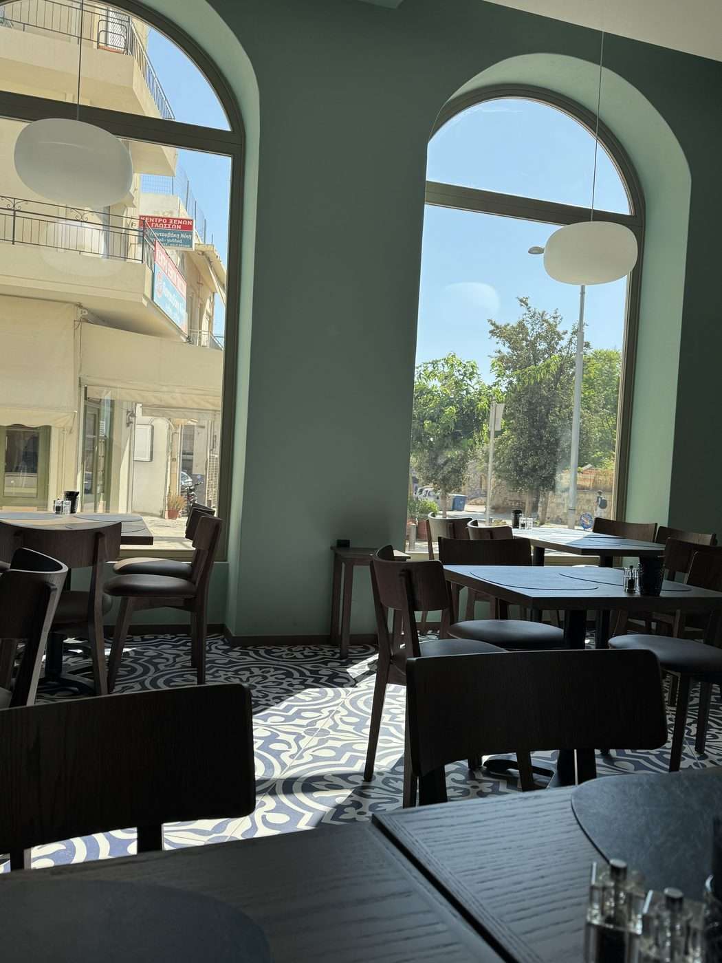 Salle du restaurant Estia à Héraklion en Crète : murs vert d'eau, grandes baies en arche, carrelage à motifs bleus et blancs et chaises en bois