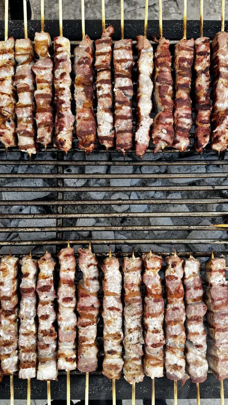 Rangées de brochettes de souvlakia en train de griller sur un grand barbecue au charbon de bois