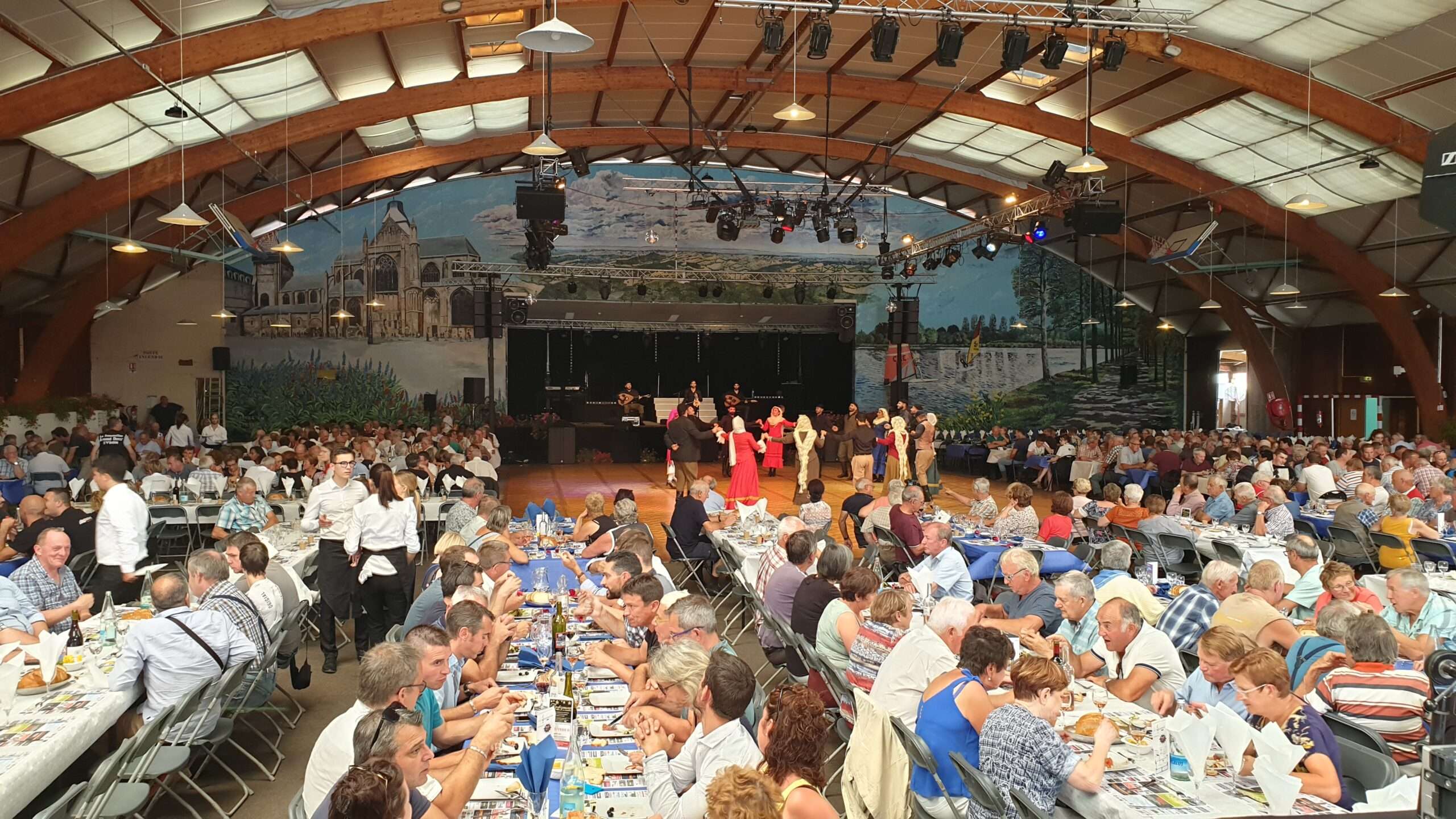 Dix ans de ponts entre la Normandie et la Crète 9 La grande salle du festival de la viande d'Évron pleine de tables, avec les danseurs crétois, août 2019