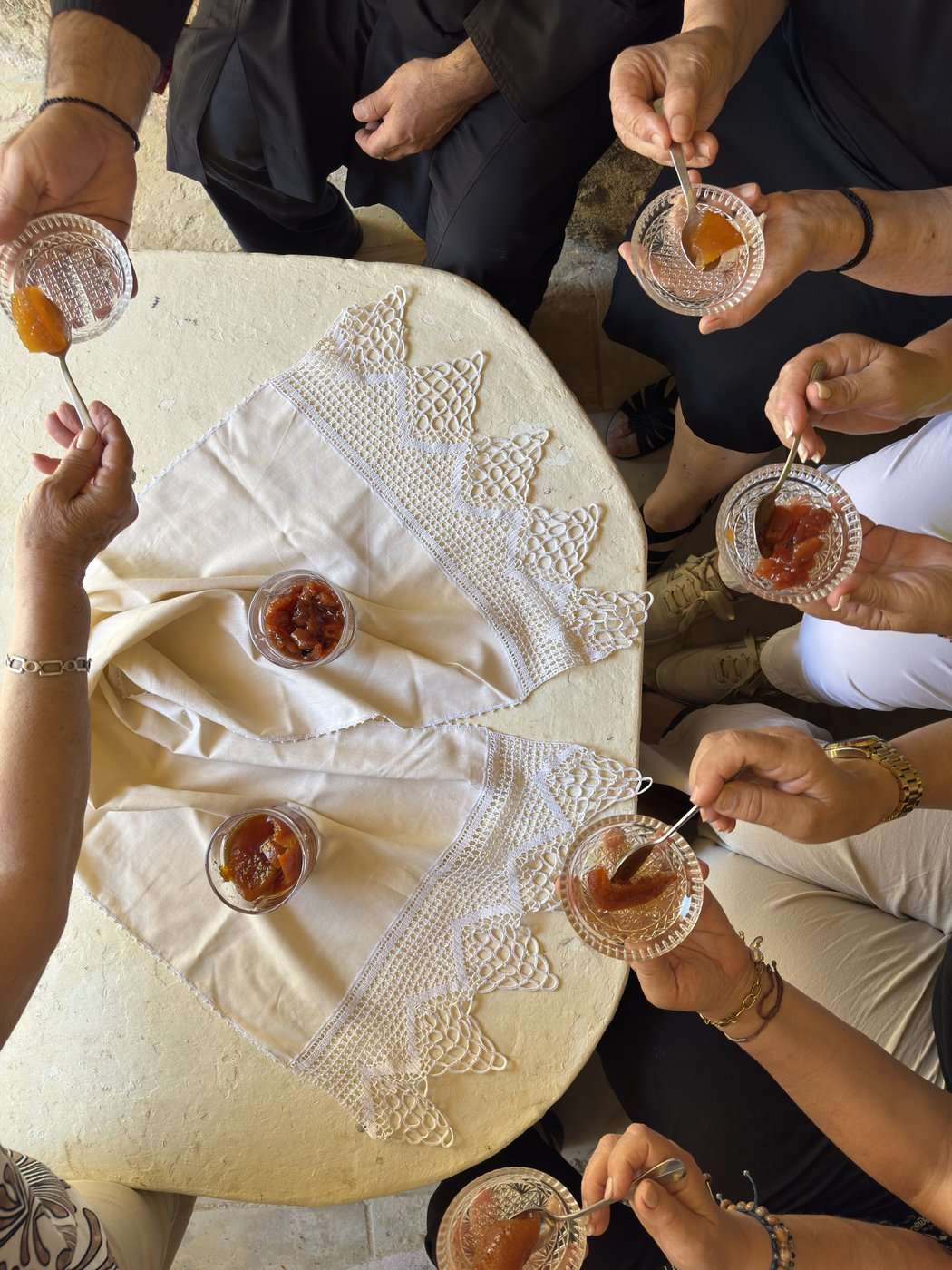 Grèce vegan, mon livre : la visite en avant-première, trois jours avant sa sortie 19 Des mains tiennent des petits verres de glyko tou koutaliou sur une nappe en dentelle, en Crète