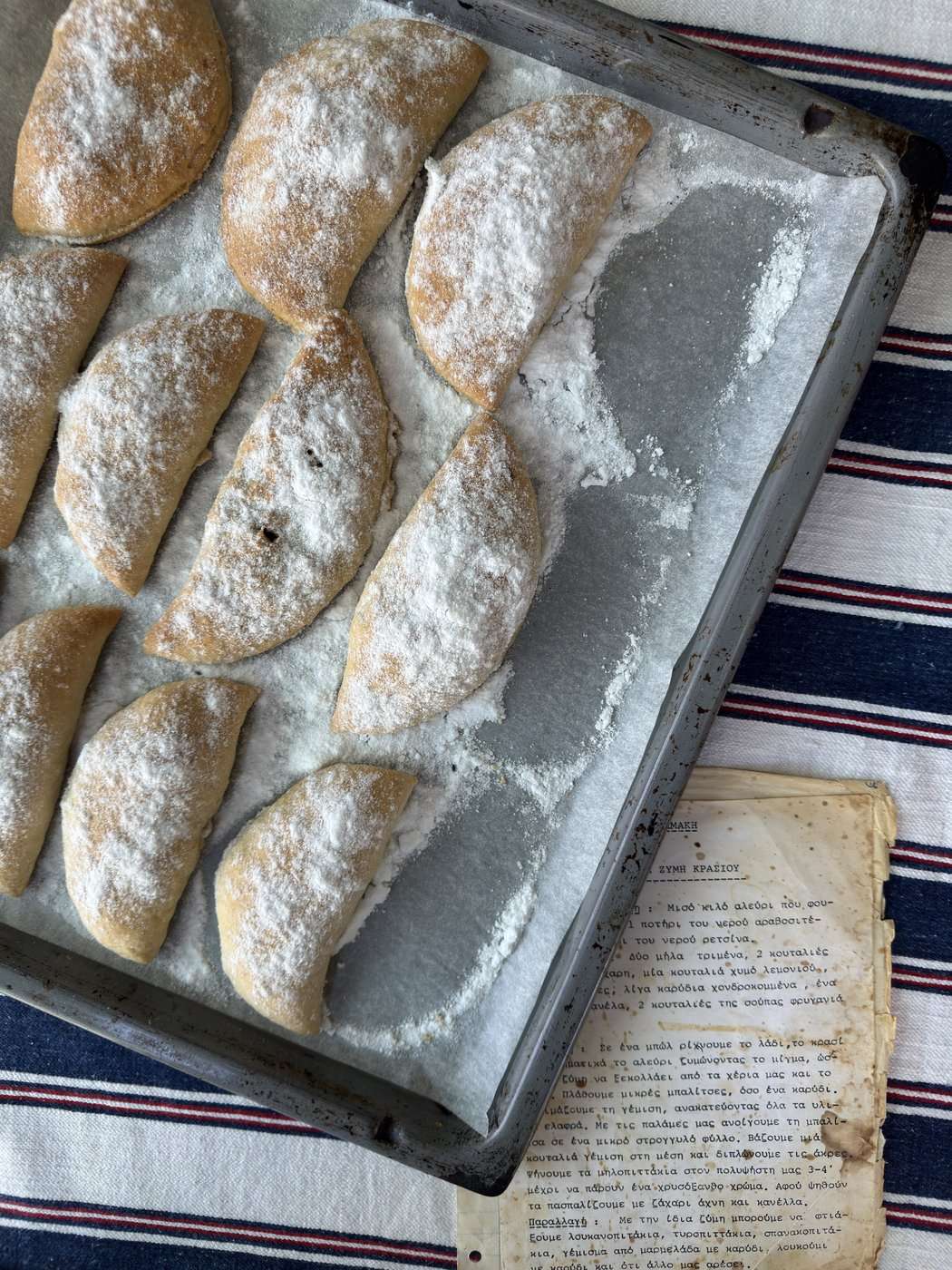 Grèce vegan, mon livre : la visite en avant-première, trois jours avant sa sortie 20 Des petits chaussons saupoudrés de sucre glace sur une plaque, posée sur un vieux cahier de recettes manuscrit