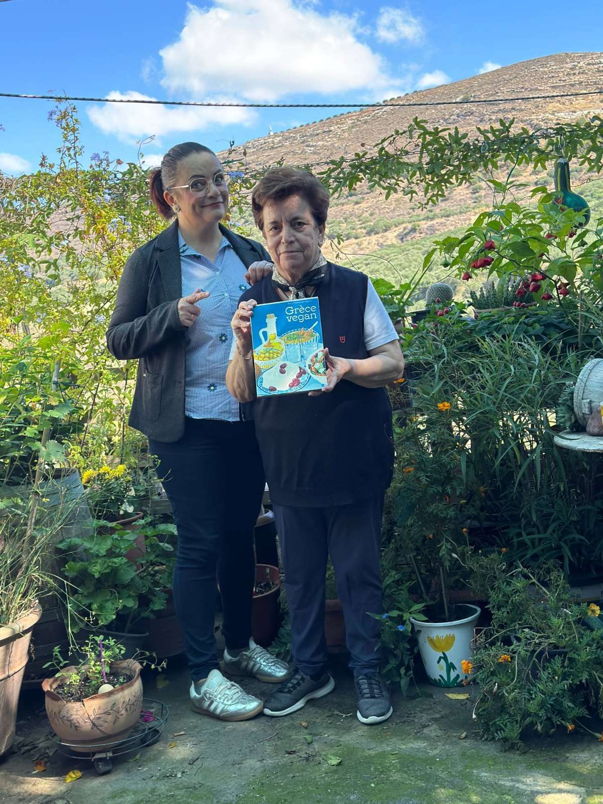 Grèce vegan, mon livre : la visite en avant-première, trois jours avant sa sortie 15 La maman de Maria tient le livre Grèce vegan dans son jardin, avec la montagne derrière